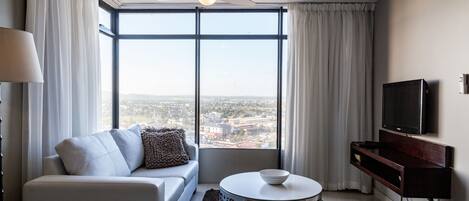A modern living room with a sofa, a round coffee table, a TV, and a large window with a city view.