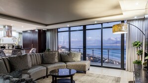 Ein modernes Wohnzimmer mit einem großen Ecksofa, einem Couchtisch und Blick auf eine Skyline durch große Fenster.