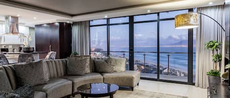 A modern living room with a large sectional sofa, a coffee table, and a view of a cityscape through large windows.