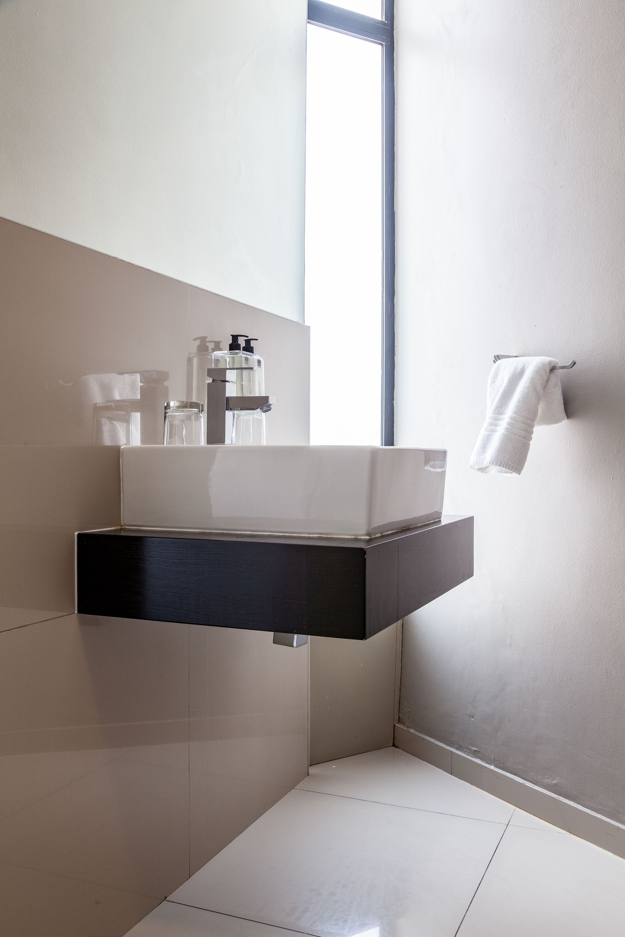 A modern bathroom with a floating white sink, a towel rack, and a large window providing natural light.