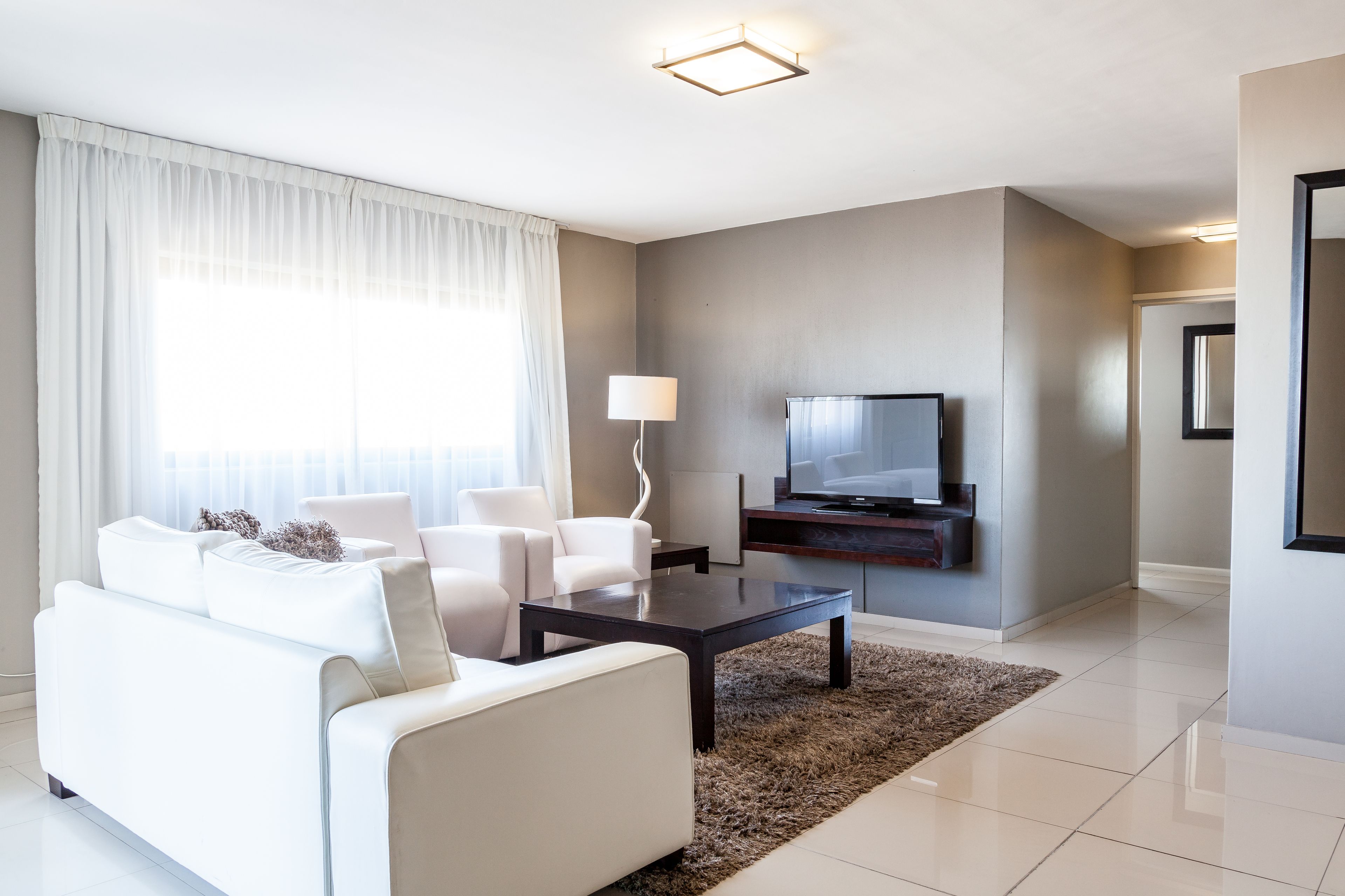 Ein modernes Wohnzimmer mit einer Couch, Sesseln, einem Couchtisch, einem Fernseher und einer Lampe.