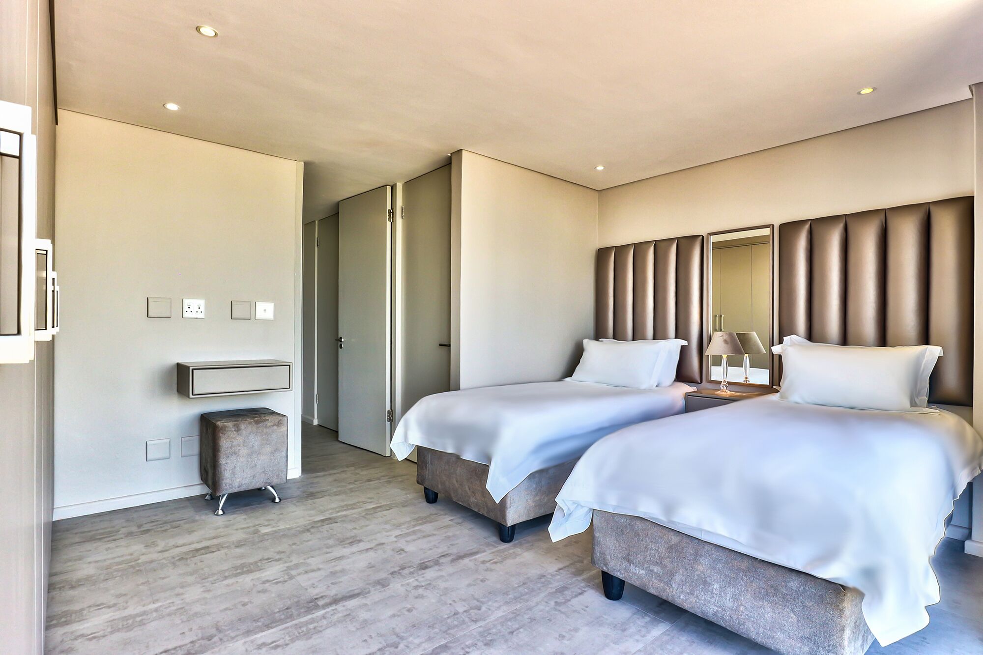 A modern hotel room with two beds, a small seating area, and a mirror on the wall.