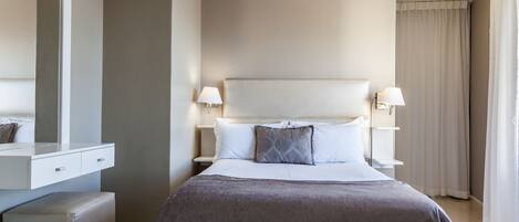 Habitación de hotel con una cama grande, dos lámparas de noche, una mesita de noche, un espejo y una ventana con cortinas.