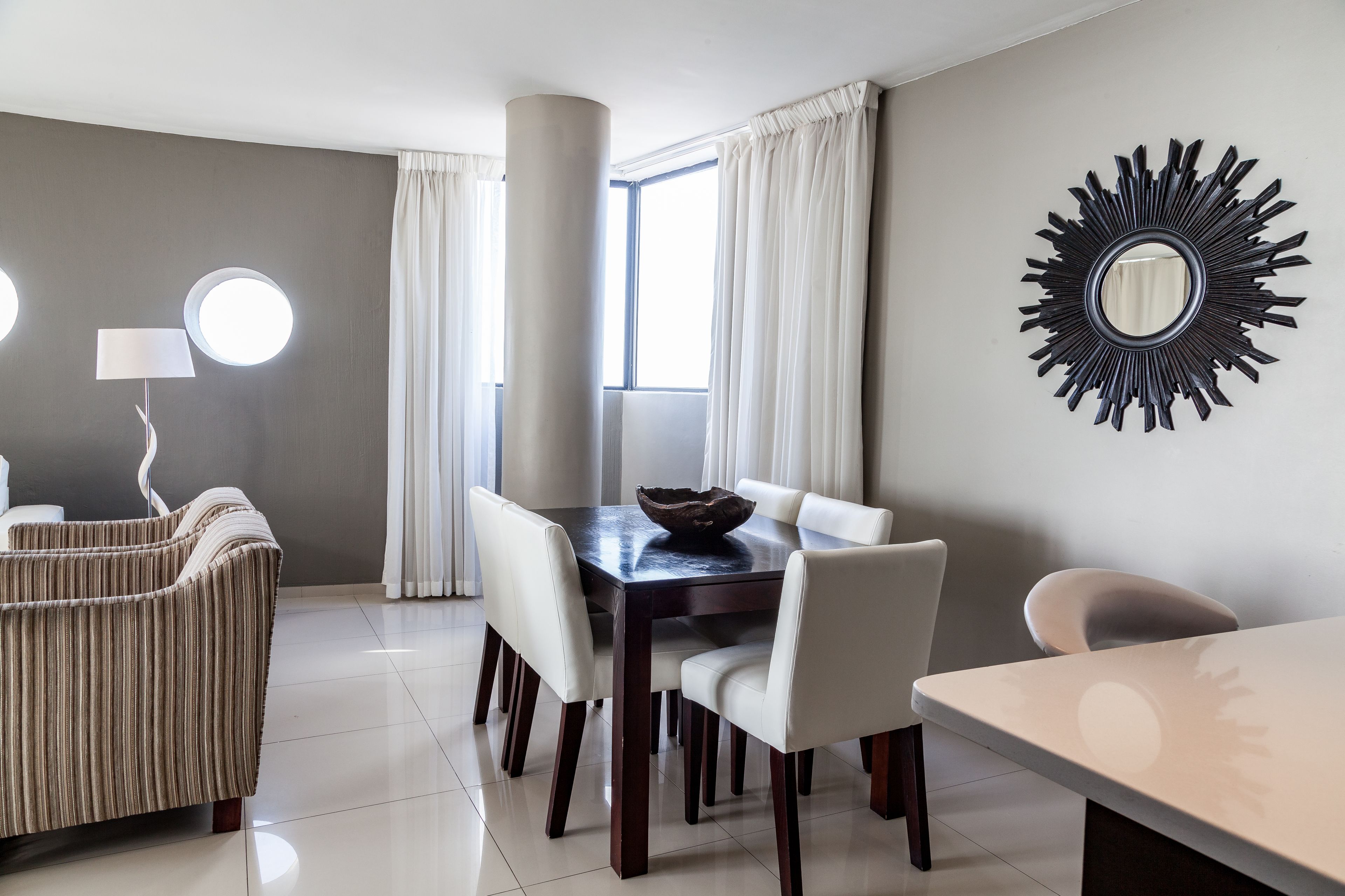 A modern dining area with a dark wooden table, white chairs, and a decorative mirror on the wall.