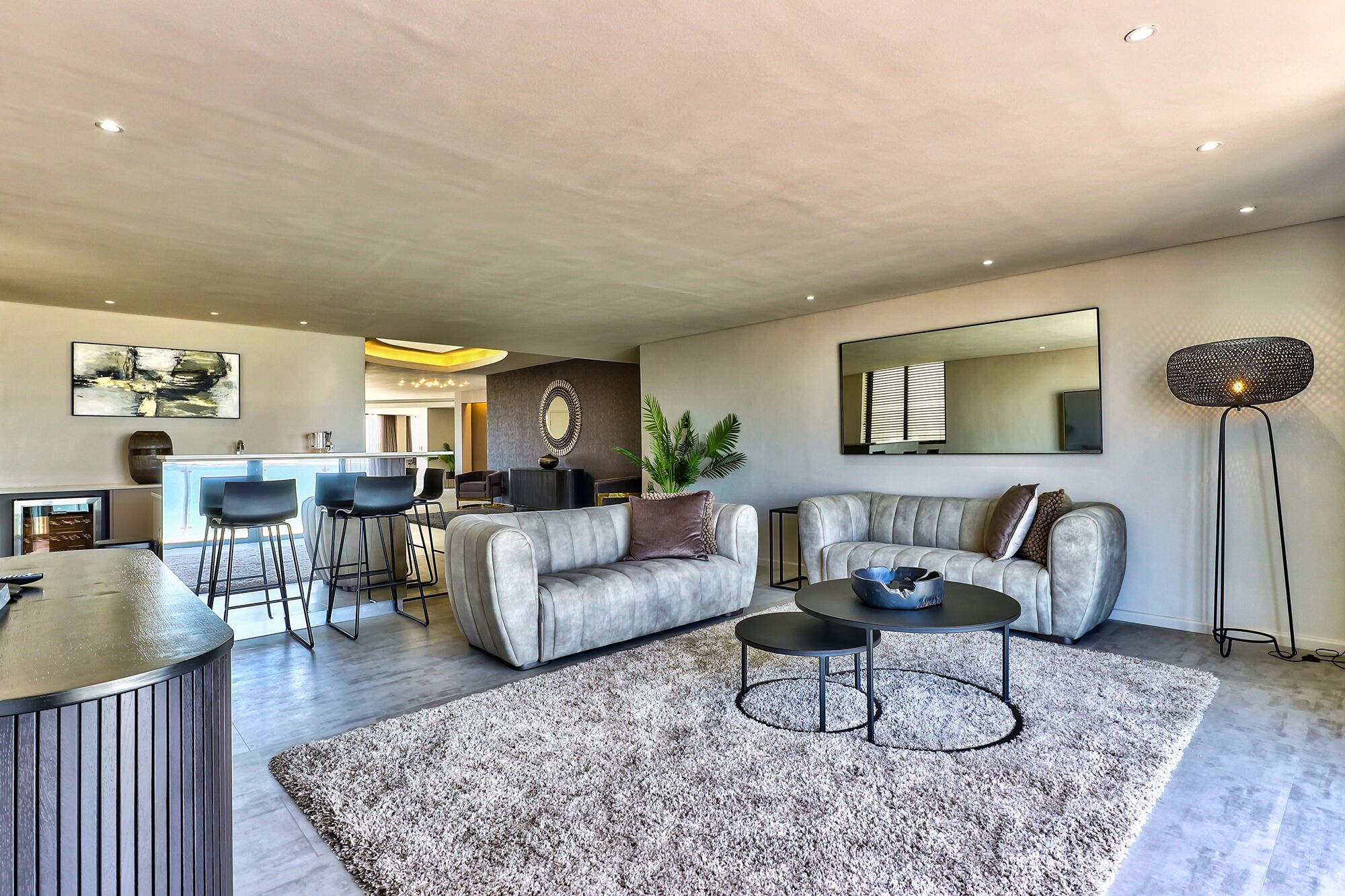 A modern living room with a grey sofa, a coffee table, and a bar area with stools.