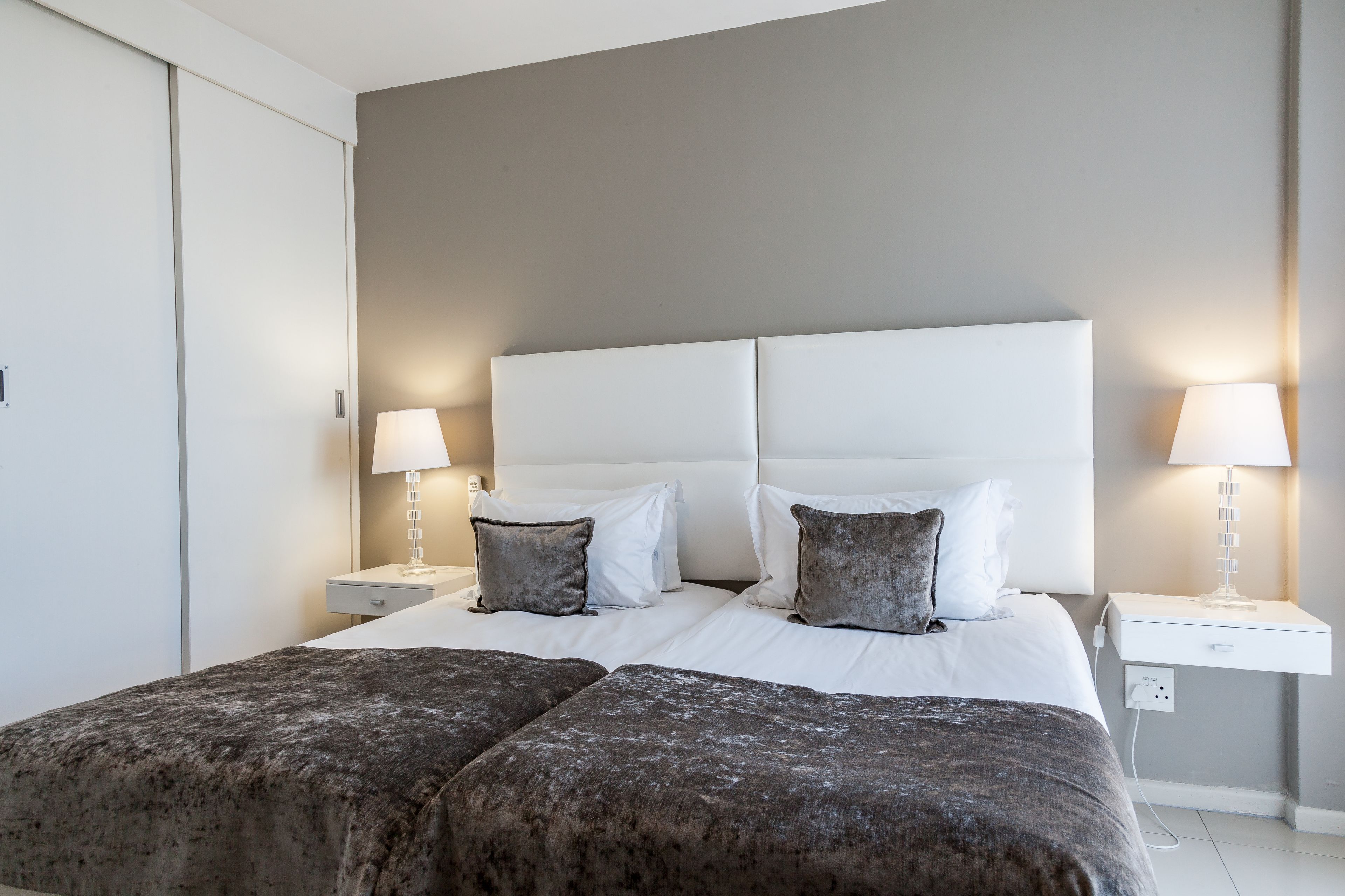Ein modernes Hotelzimmer mit einem großen Bett, zwei Nachttischen mit Lampen und einer neutralen Farbgestaltung.