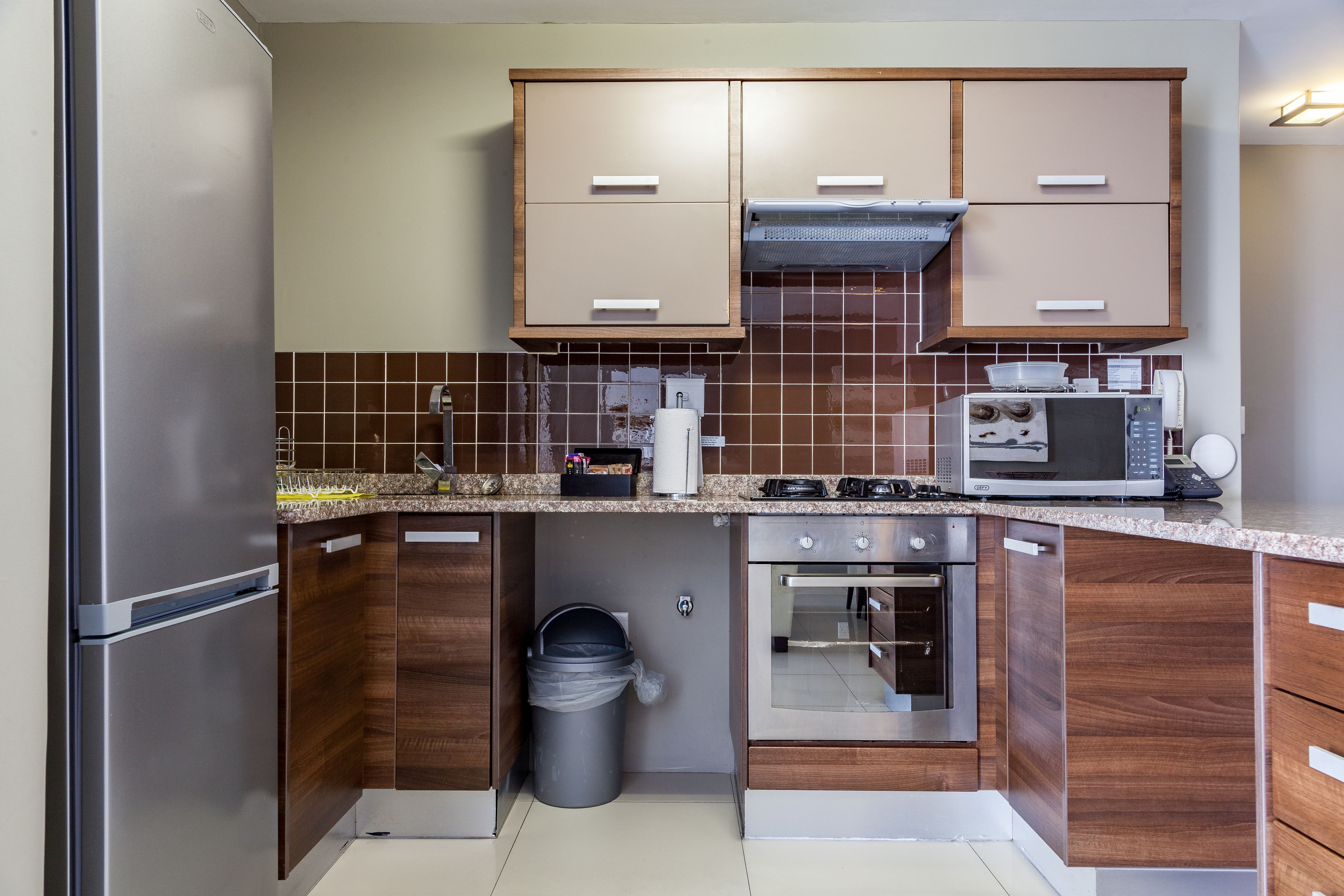 A compact kitchen with wooden cabinets, a stainless steel refrigerator, a microwave, and an oven.