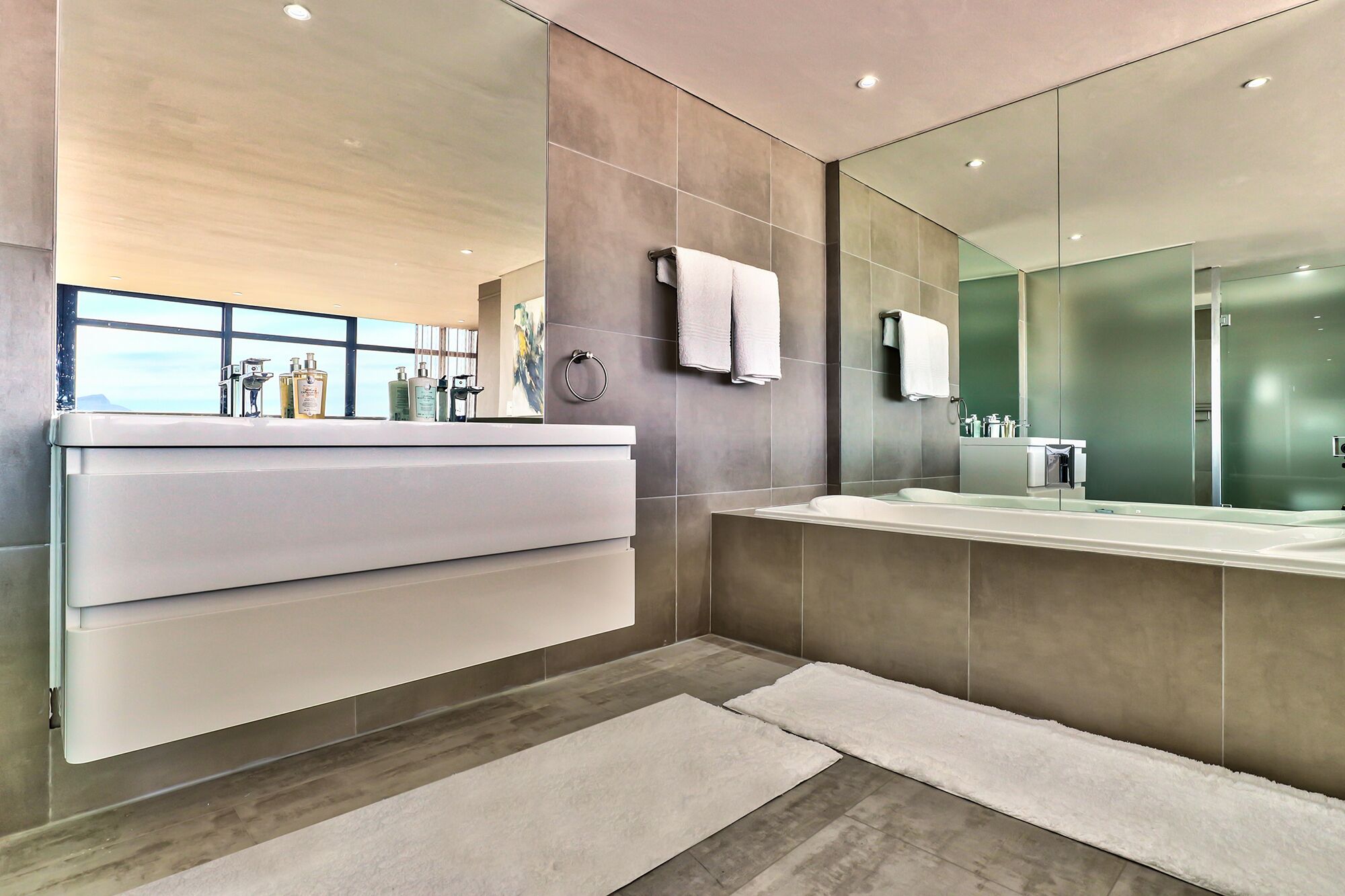 A modern bathroom with a large mirror, two sinks, and a vanity with toiletries.