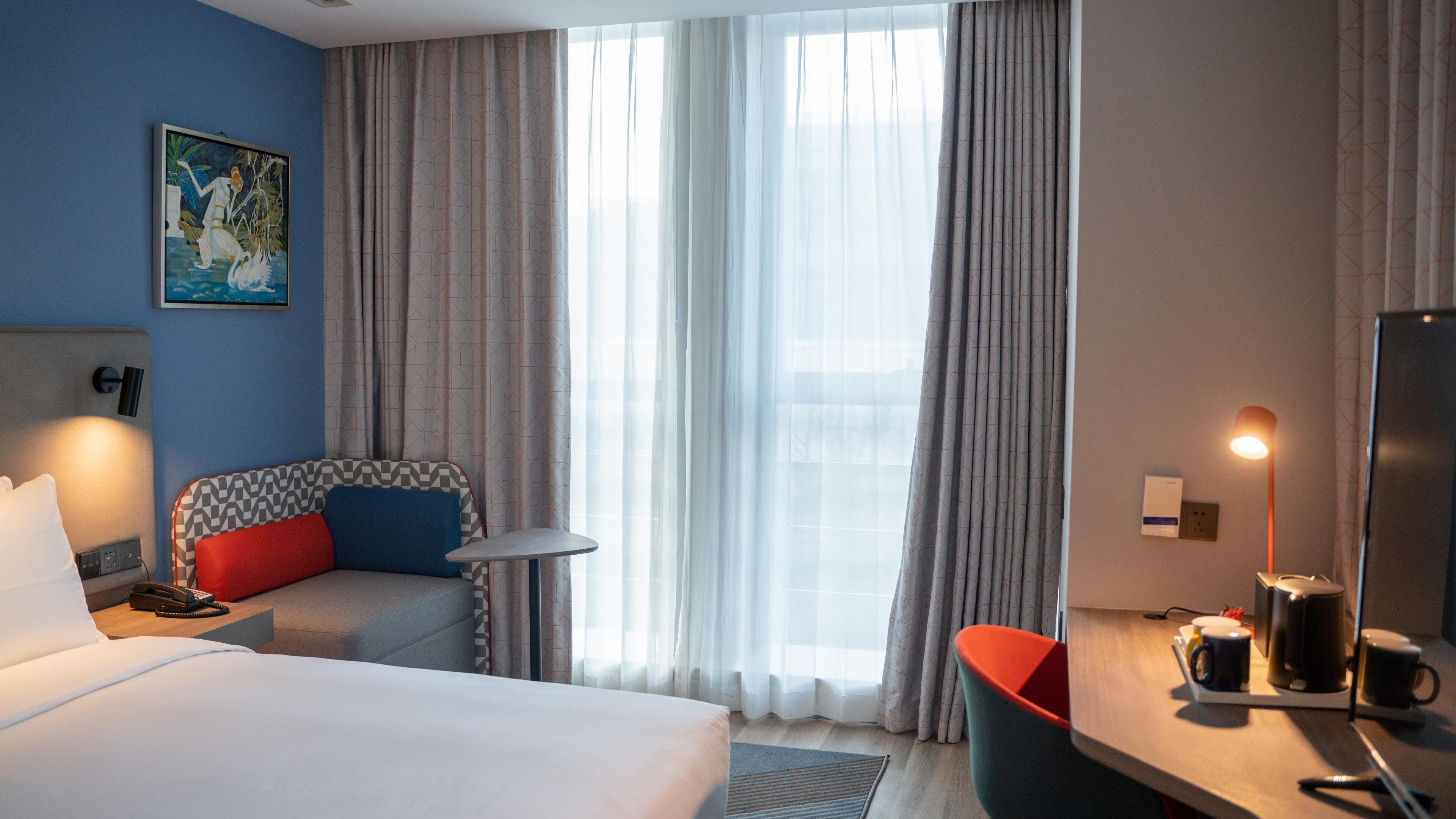 Habitación de hotel con una cama, un escritorio con silla, un teléfono y un cuadro en la pared.