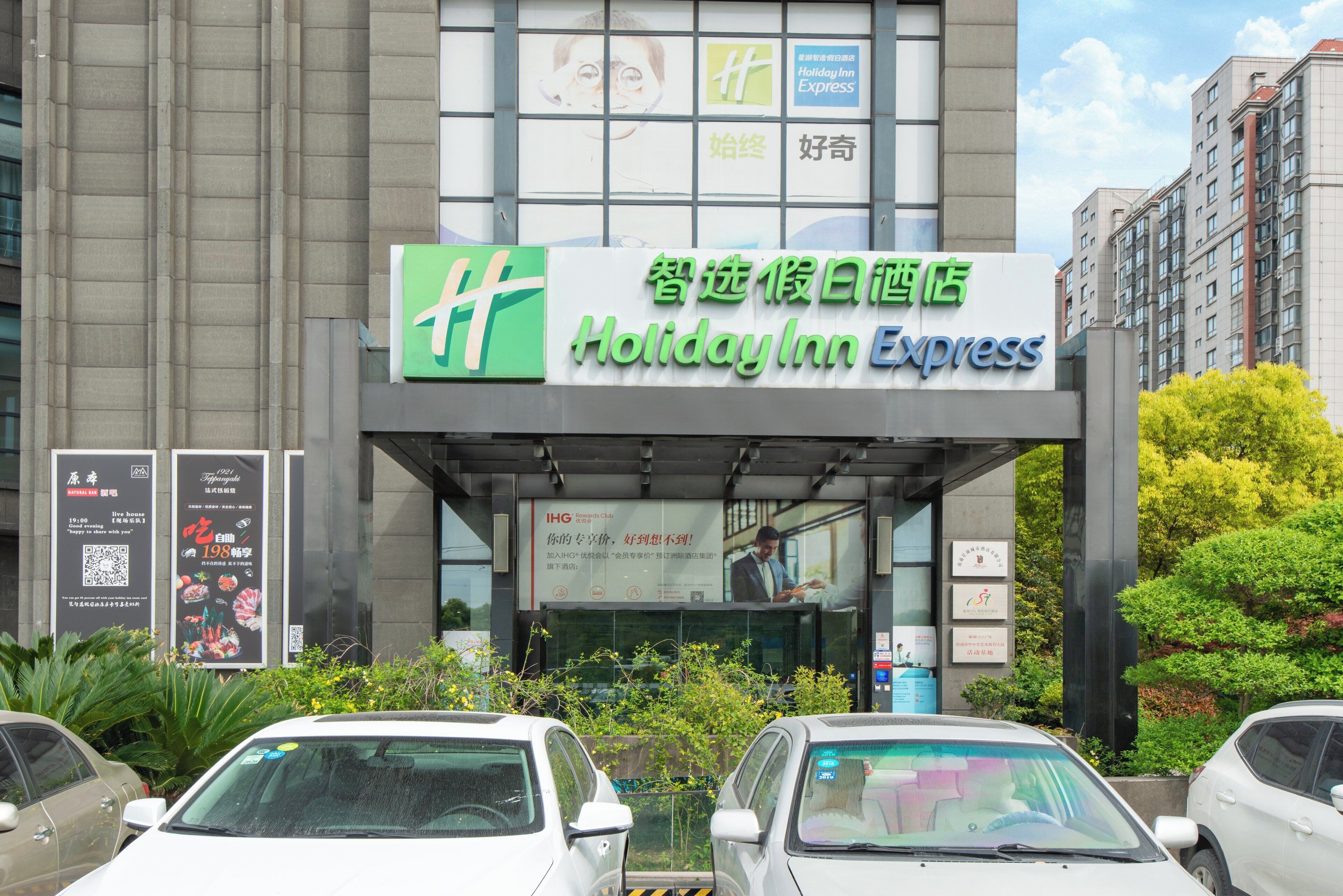 A Holiday Inn Express hotel with a clear entrance, signage in multiple languages, and a parking lot with several cars.