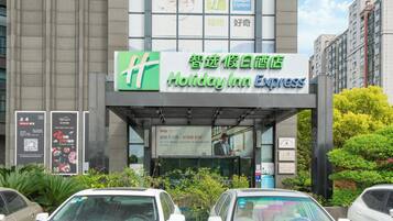 A Holiday Inn Express hotel with a clear entrance, signage in multiple languages, and a parking lot with several cars.