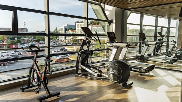Une salle de sport équipée de matériel d’exercice et dotée de grandes fenêtres donnant sur un parking.