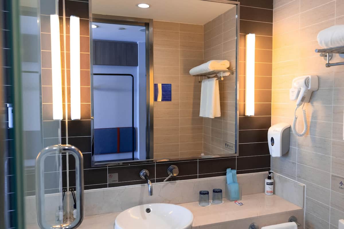 A modern bathroom with a sink, mirror, towel rack, and a hairdryer mounted on the wall.