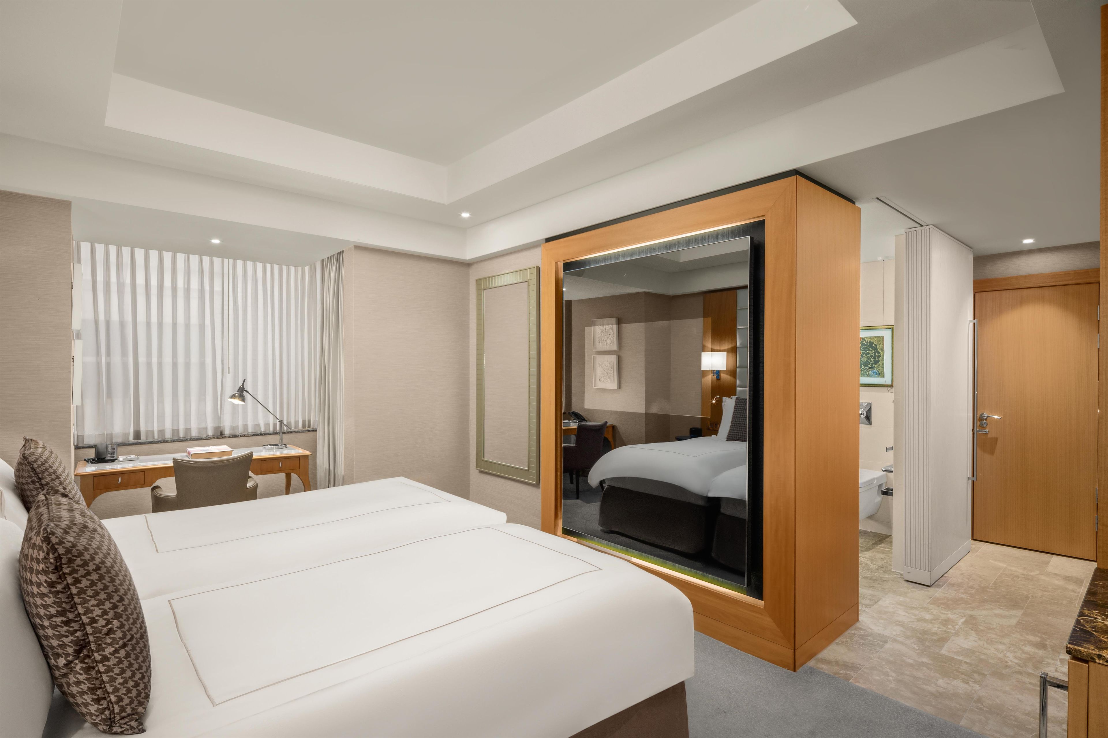 A hotel room with a large bed, a desk, a chair, a wardrobe, and a bathroom.