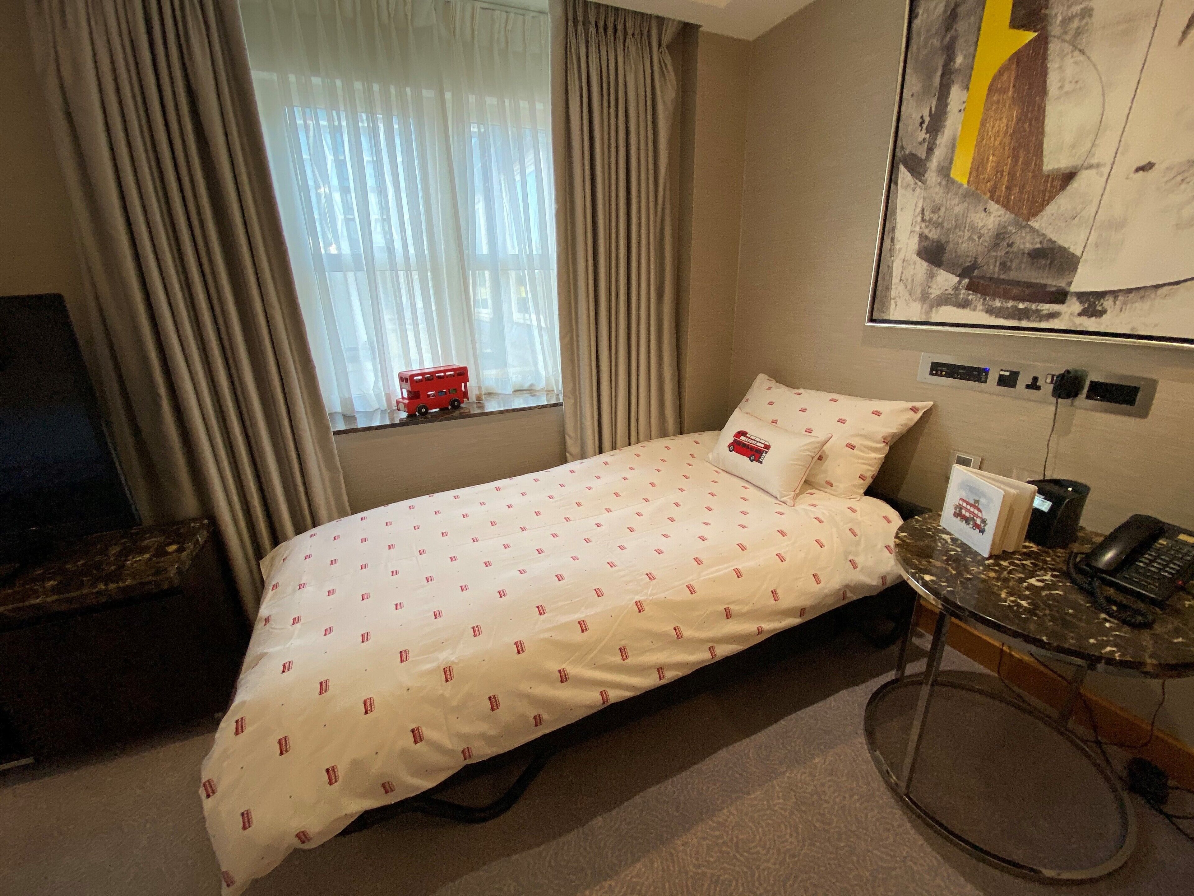 A hotel room with a bed, a desk with a computer, a chair, and a window with curtains.