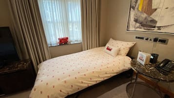 A hotel room with a bed, a desk with a computer, a chair, and a window with curtains.