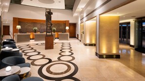 A modern hotel lobby with a reception desk, seating area, and a decorative sculpture. - Conrad London St. James (London)