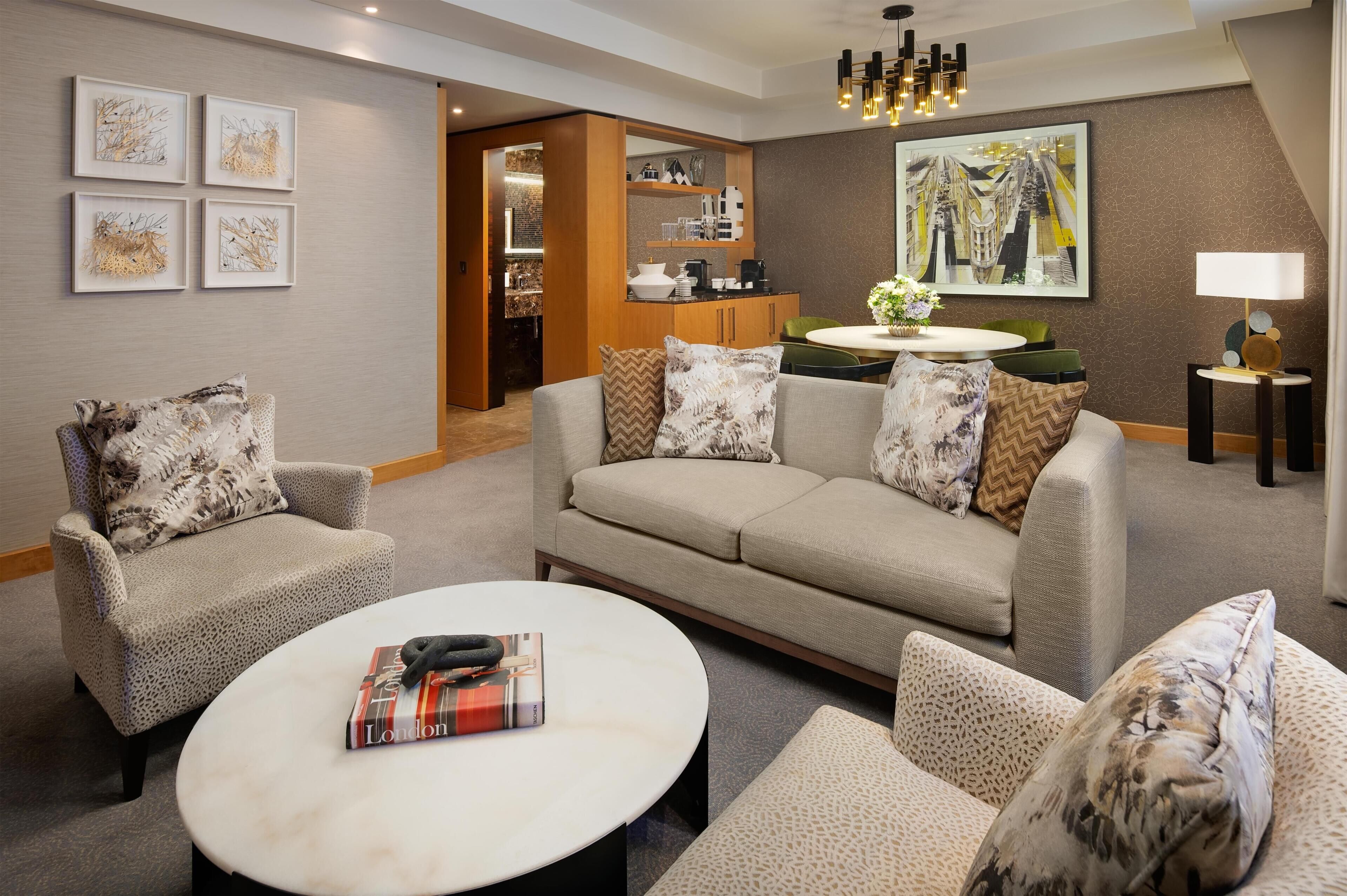 A modern living room with a sofa, armchairs, a coffee table, and a dining area with a kitchen in the background.