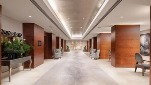 A hotel lobby with a long corridor, wooden paneling, seating areas, and a central artwork. - Conrad London St. James (London)