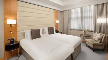A hotel room with a large bed, bedside tables, a chair, and a small table with a vase.