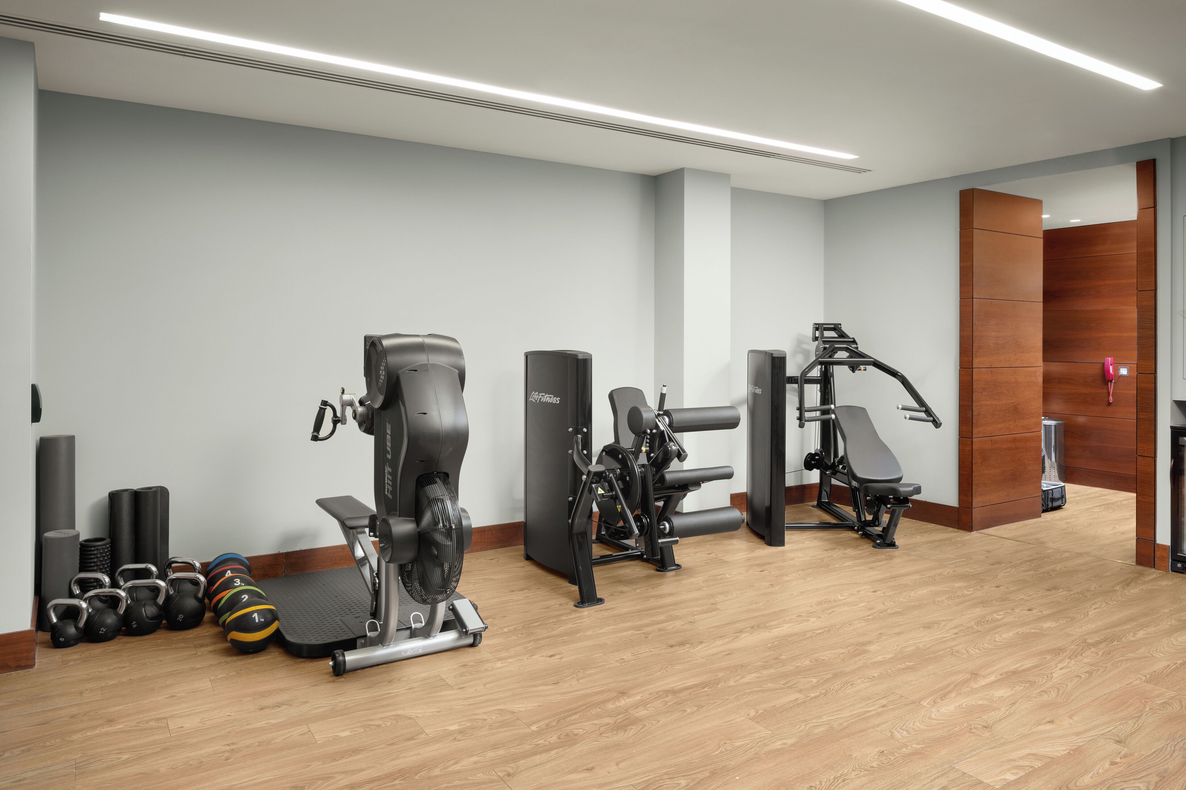 A modern gym with cardio machines, free weights, and a wooden floor.