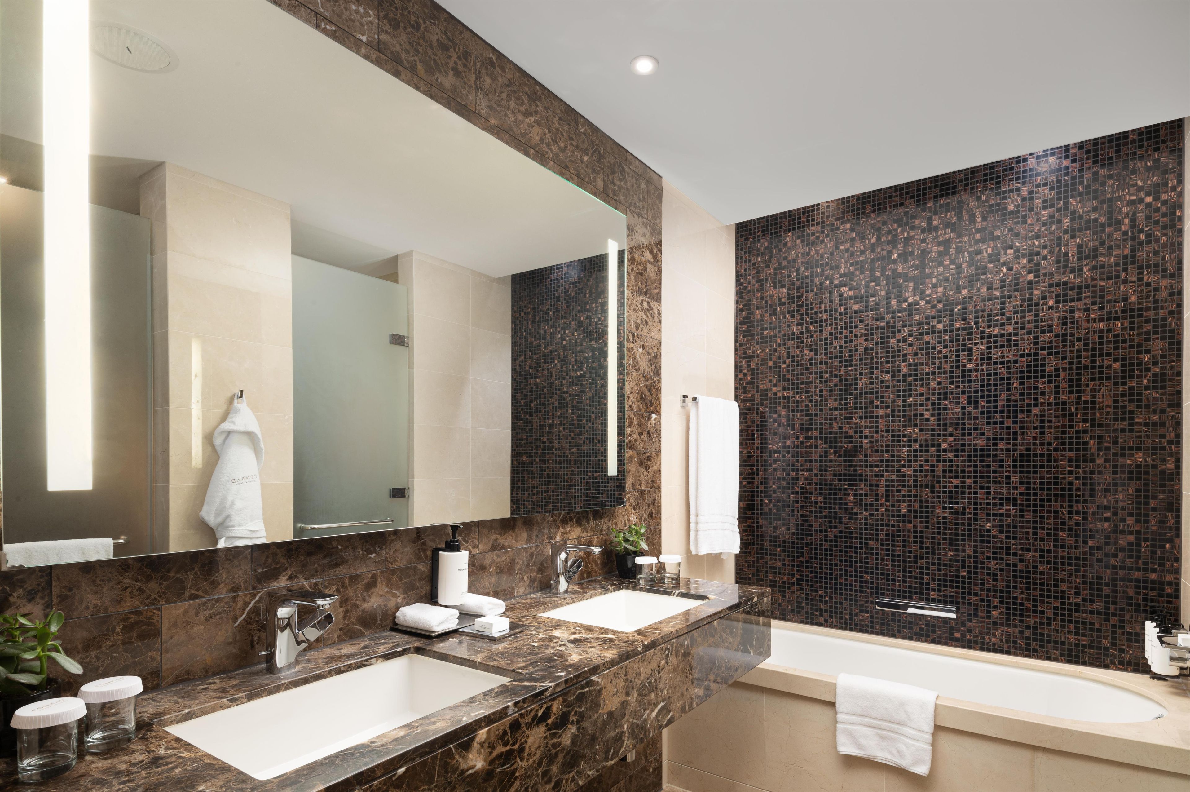 A modern bathroom with two sinks, a large mirror, and a dark mosaic wall.