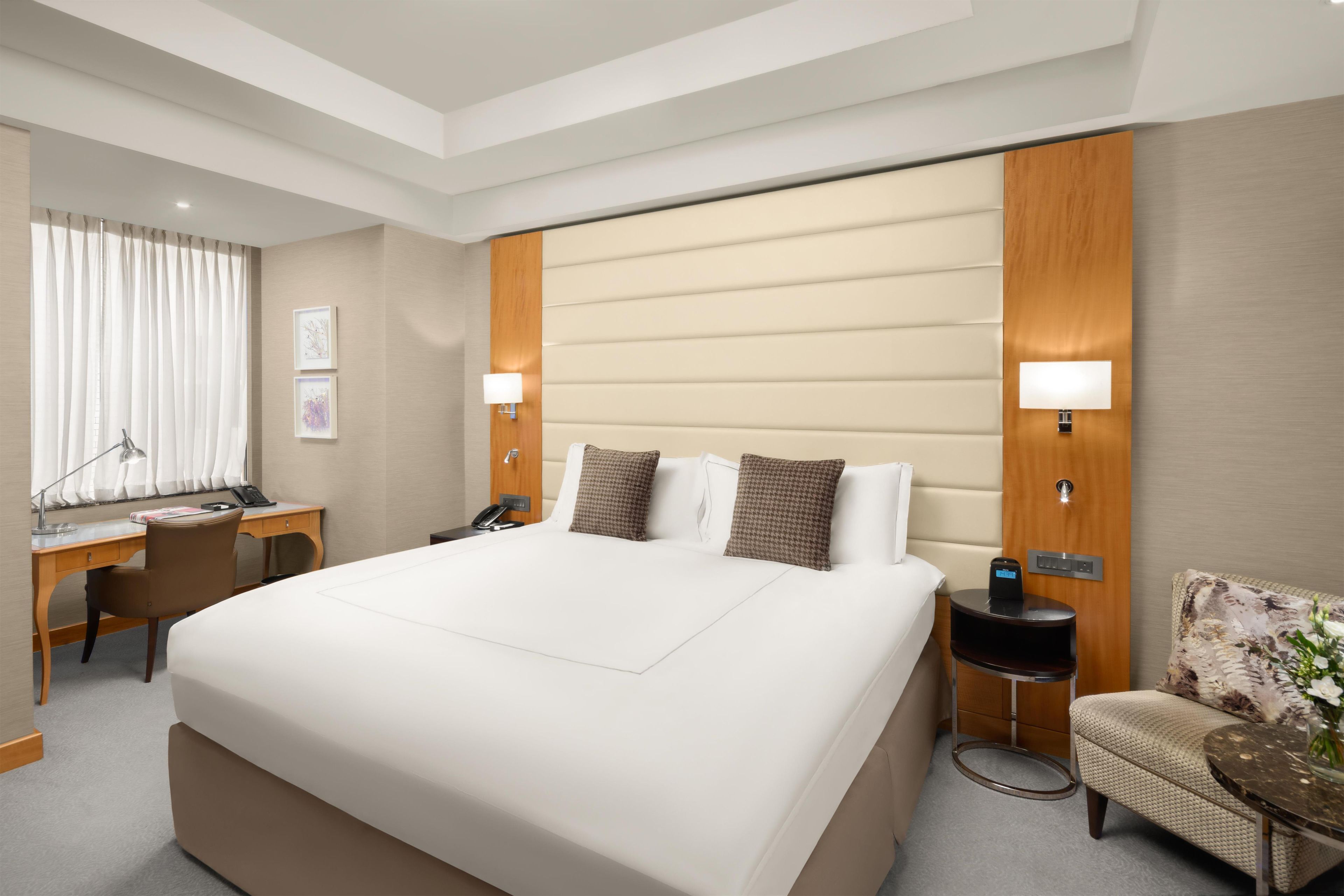 Una habitación de hotel con una cama grande, un escritorio, una silla, una mesita de noche y una lámpara.