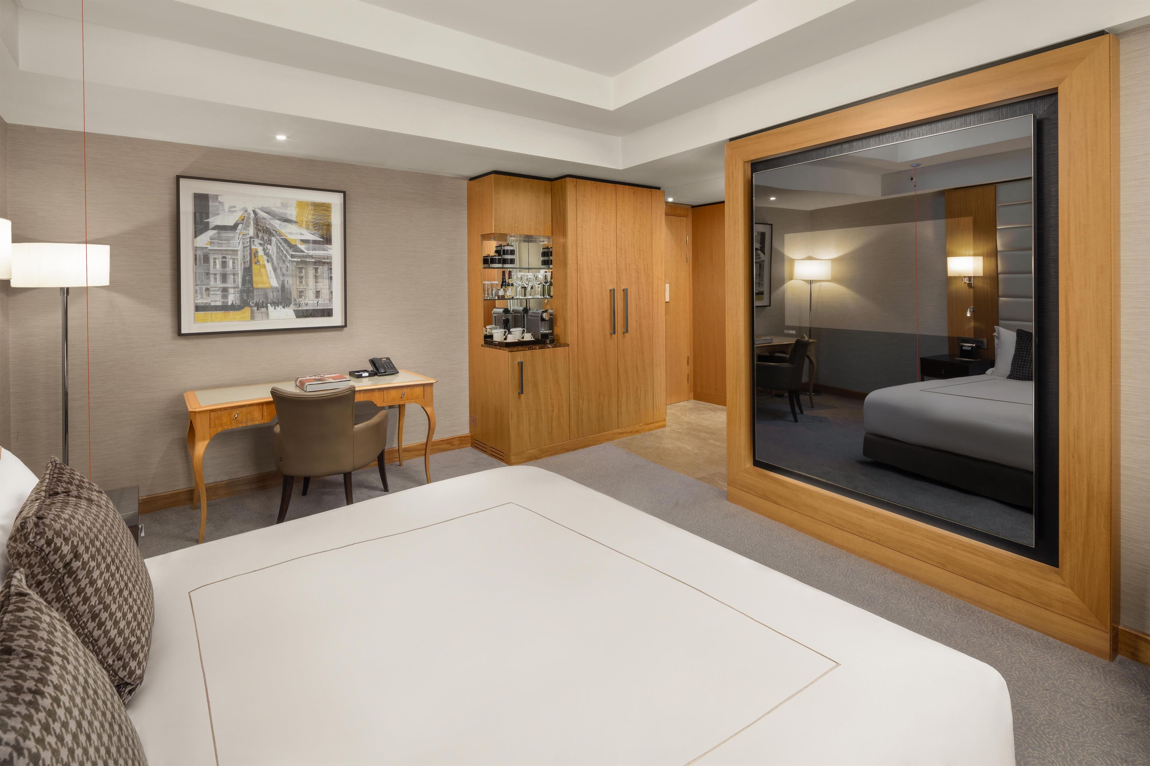 A hotel room with a bed, desk, chair, wardrobe, and a large mirror.