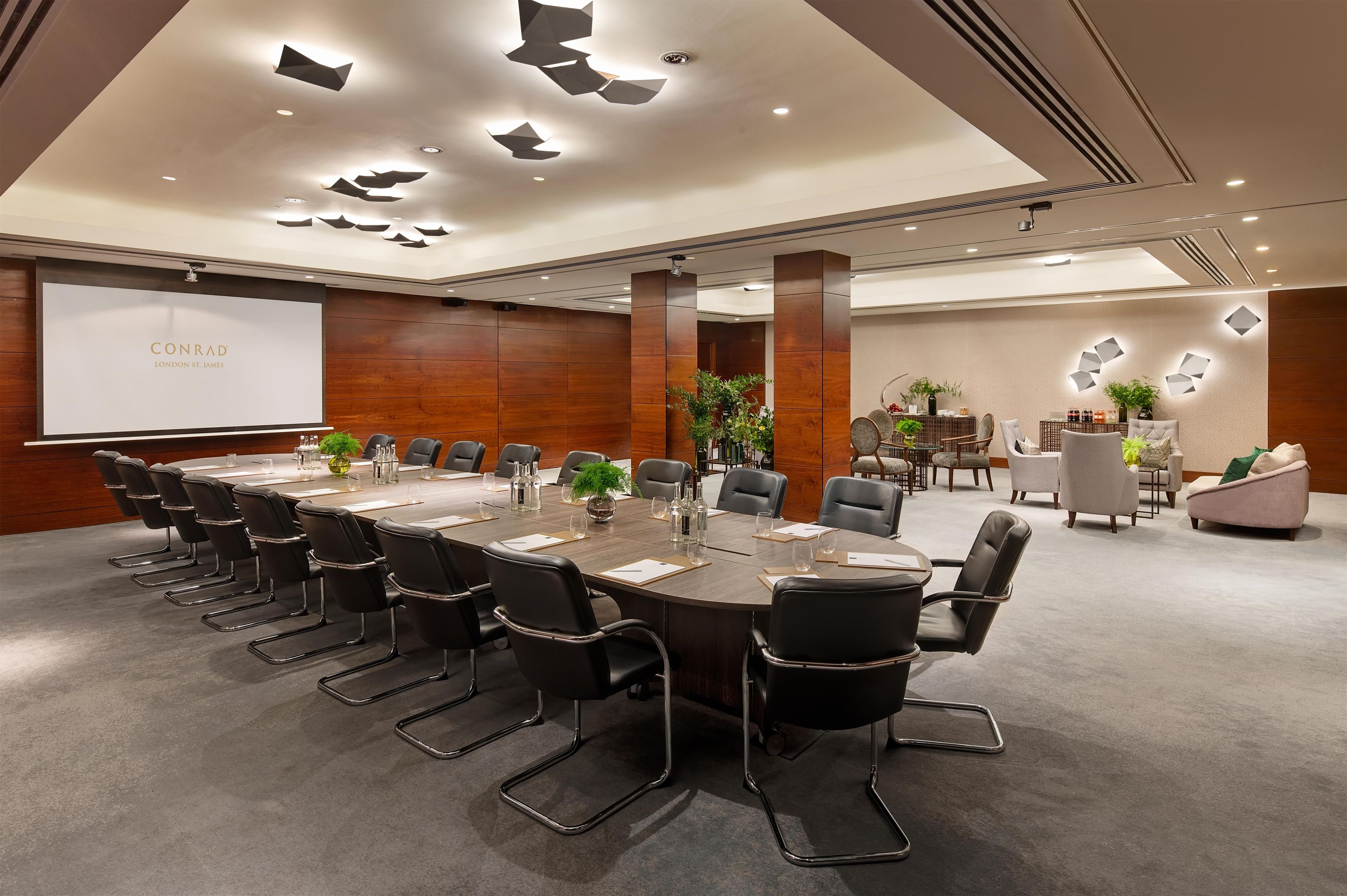 A conference room with a long table, black chairs, and a projector screen.
