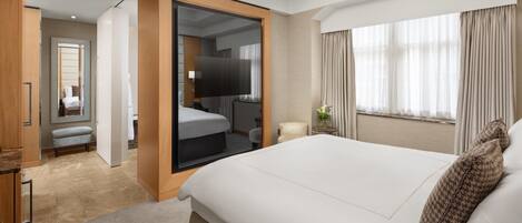 A modern hotel room with a large bed, a walk-in closet, a sitting area, and a view of the outdoors.