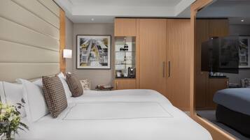 Quarto de hotel moderno com uma cama grande, televisão, pequena cozinha e um quadro na parede.
