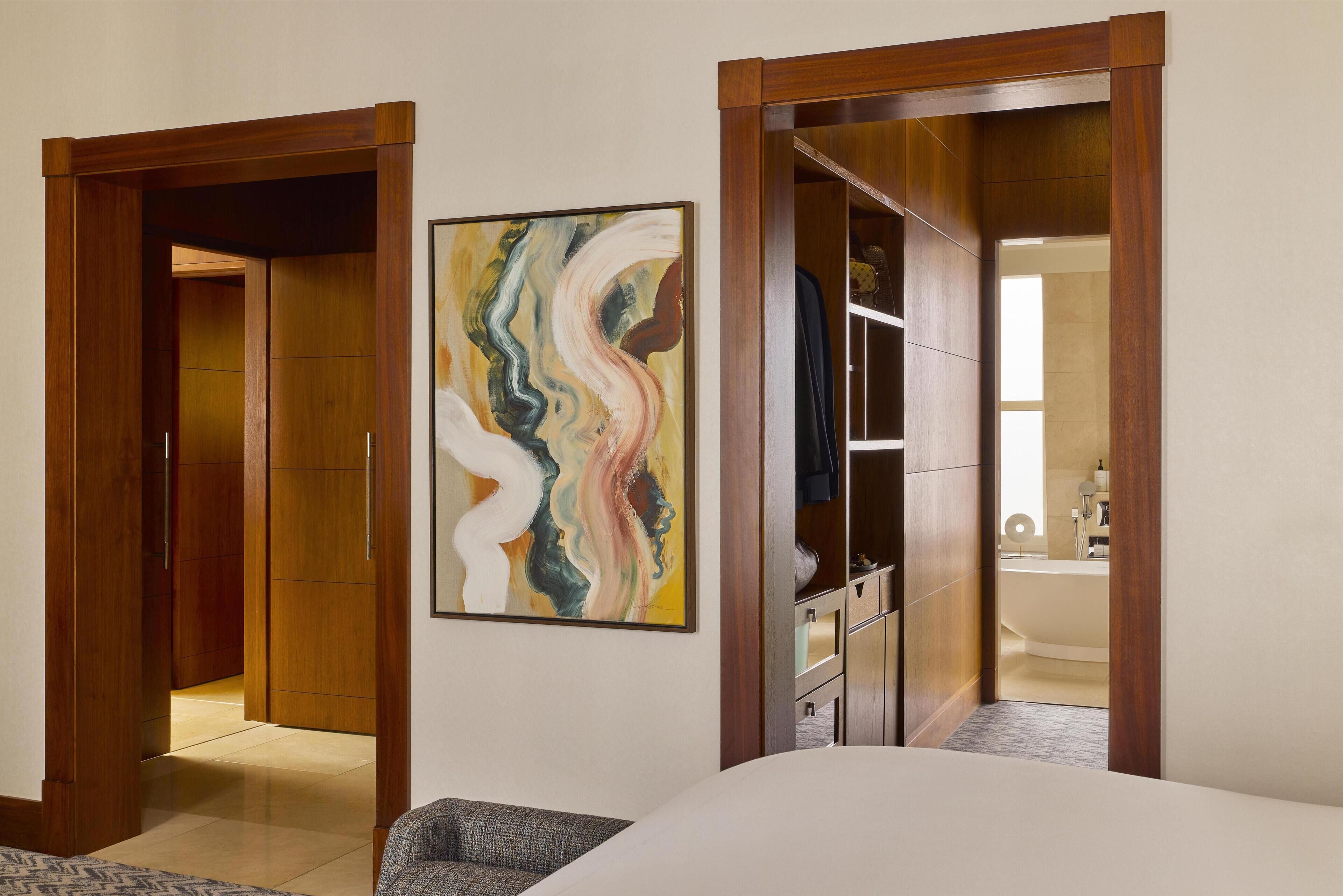 A bedroom with a bed, a wooden wardrobe, a bathroom with a bathtub, and a painting on the wall.