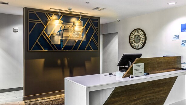 A reception desk with a modern design, a clock on the wall, and a sign indicating check-in times. - Holiday Inn Express Salinas by IHG (Salina)