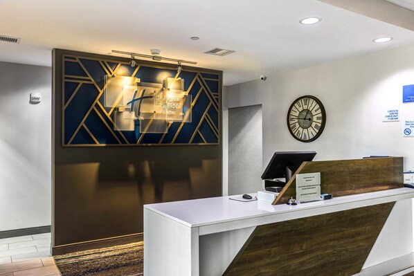 A reception desk with a modern design, a clock on the wall, and a sign indicating check-in times.
