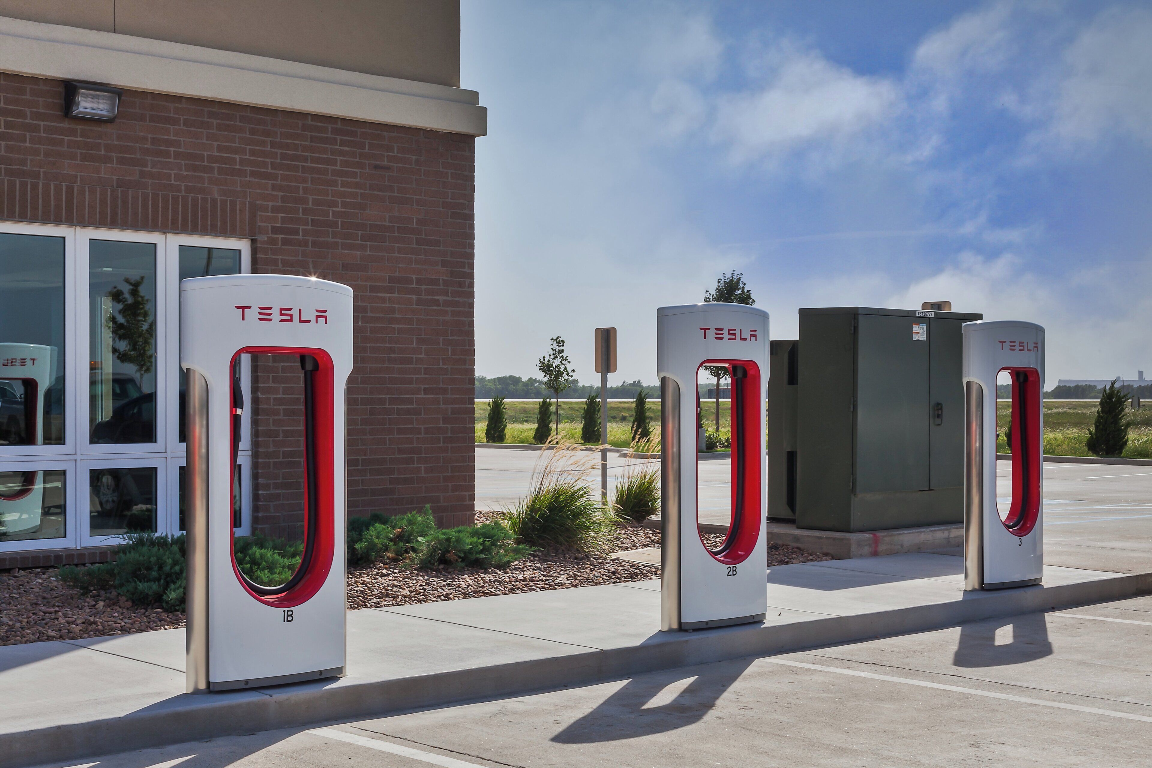 Three Tesla charging stations in front of a building with a brick facade.
