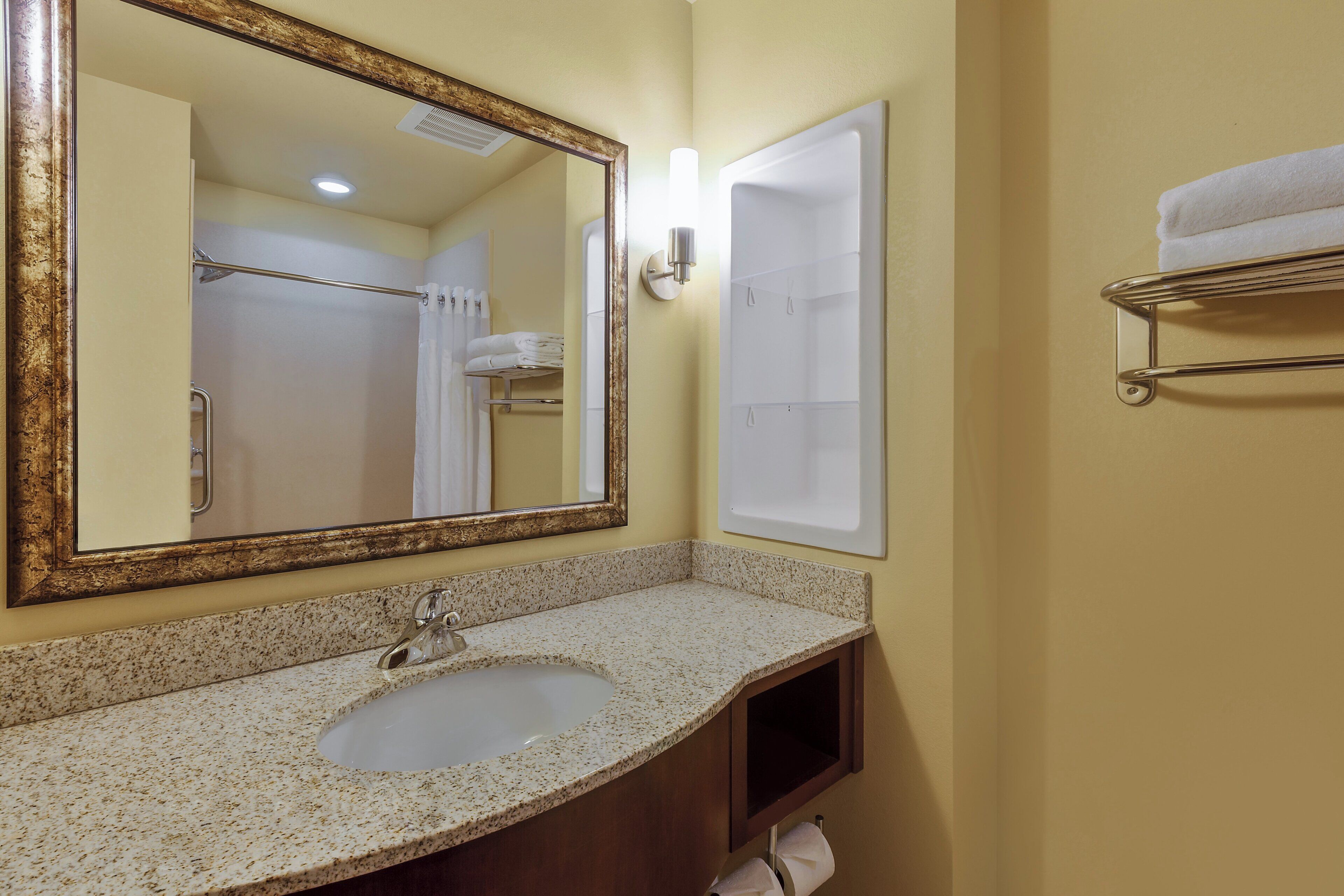 A bathroom with a sink, mirror, towel rack, and shower area.