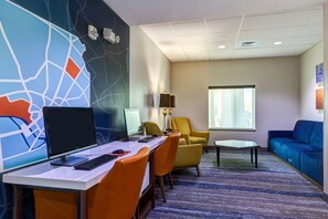 A hotel room with a desk, computer, chairs, a sofa, a lamp, and a large window.