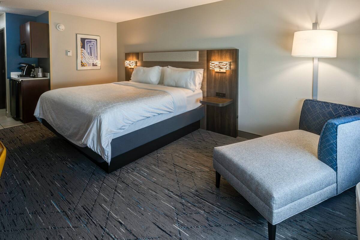 Ett hotellrum med en stor säng, en stol, ett skrivbord och en lampa.