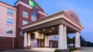 A Holiday Inn Express & Suites building with a covered entrance, brick facade, and a clear sky.