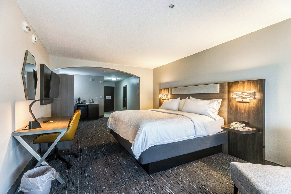 A hotel room with a bed, desk, chair, and a TV.