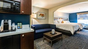 A hotel room with a kitchenette, a bed, a sofa, and a small table.
