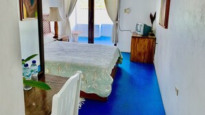 A bedroom with a bed, a nightstand, a lamp, a TV, and a view of the outdoors. - Hotel Rio Bueno (Rio Bueno)