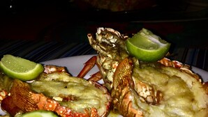 A plate of cooked lobsters with lime wedges and a yellow sauce. - Hotel Rio Bueno (Rio Bueno)