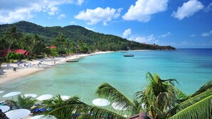 Une plage avec une eau turquoise et limpide, des palmiers et un bateau.
