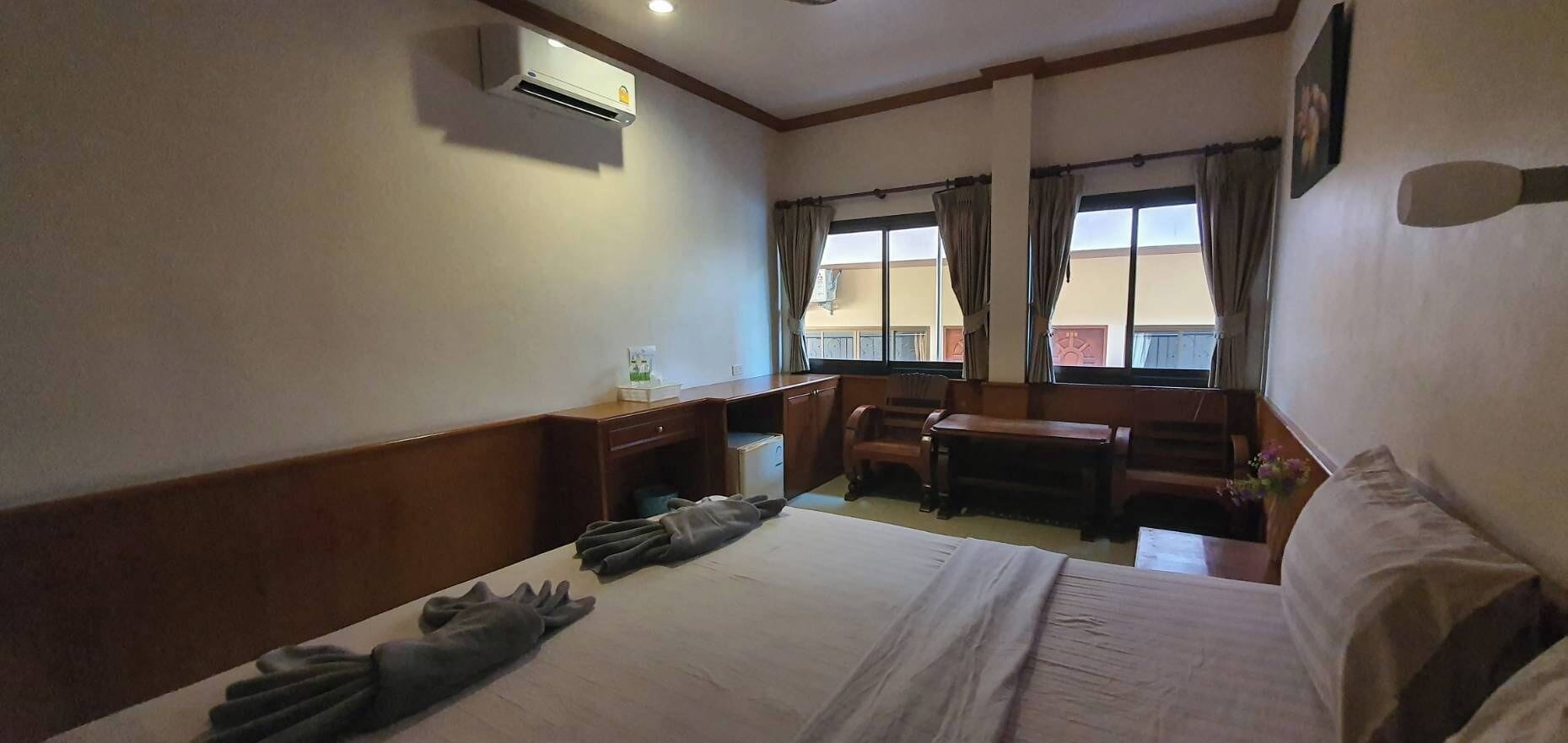 A hotel room with a bed, a desk, a chair, and an air conditioning unit.