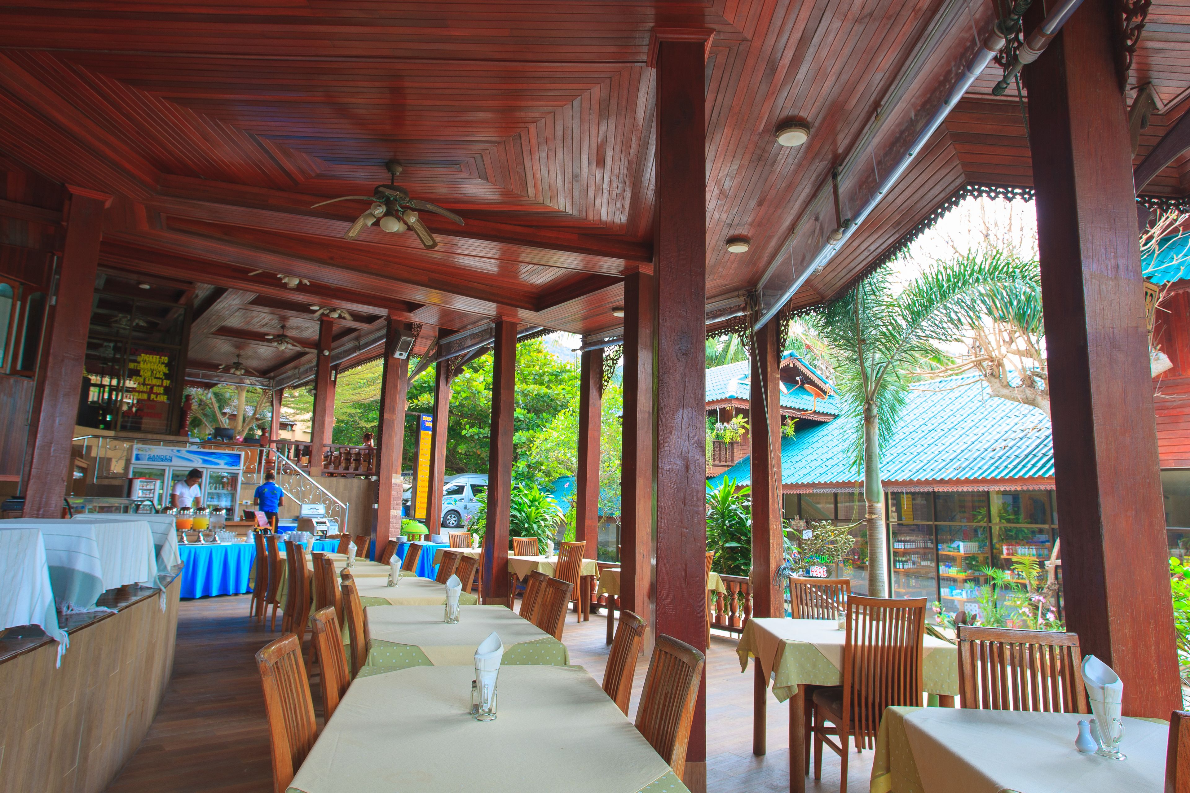 A restaurant with wooden tables and chairs, a bar area, and a view of greenery outside.