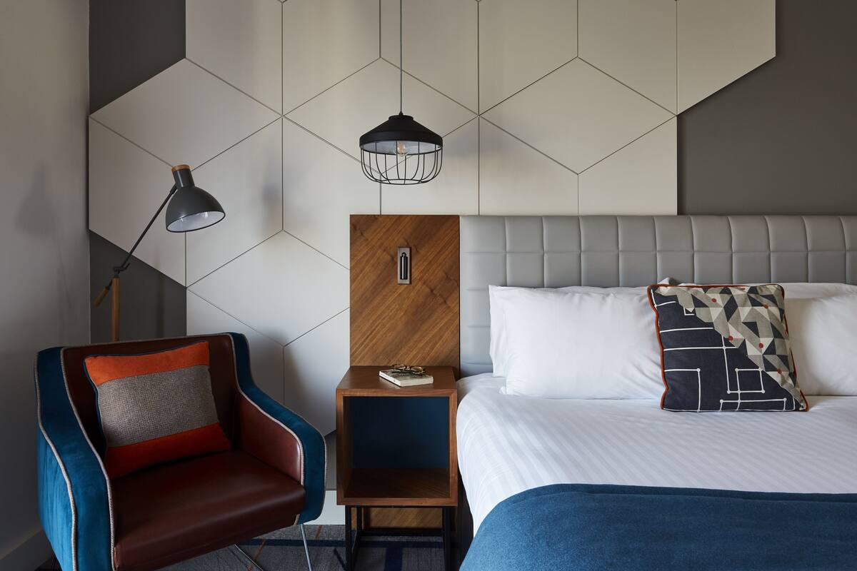 Ein modernes Hotelzimmer mit Bett, Nachttisch, Stuhl und Lampe.