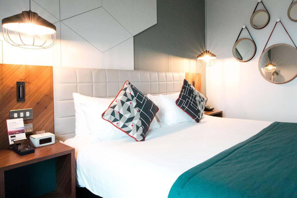 Ein Hotelzimmer mit einem Bett, zwei Nachttischen, einem Wandspiegel und einer Wandleuchte.