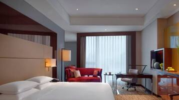 Ein Hotelzimmer mit einem großen Bett, einem Schreibtisch, einem Stuhl, einem Fernseher und einem Fenster mit Vorhängen.