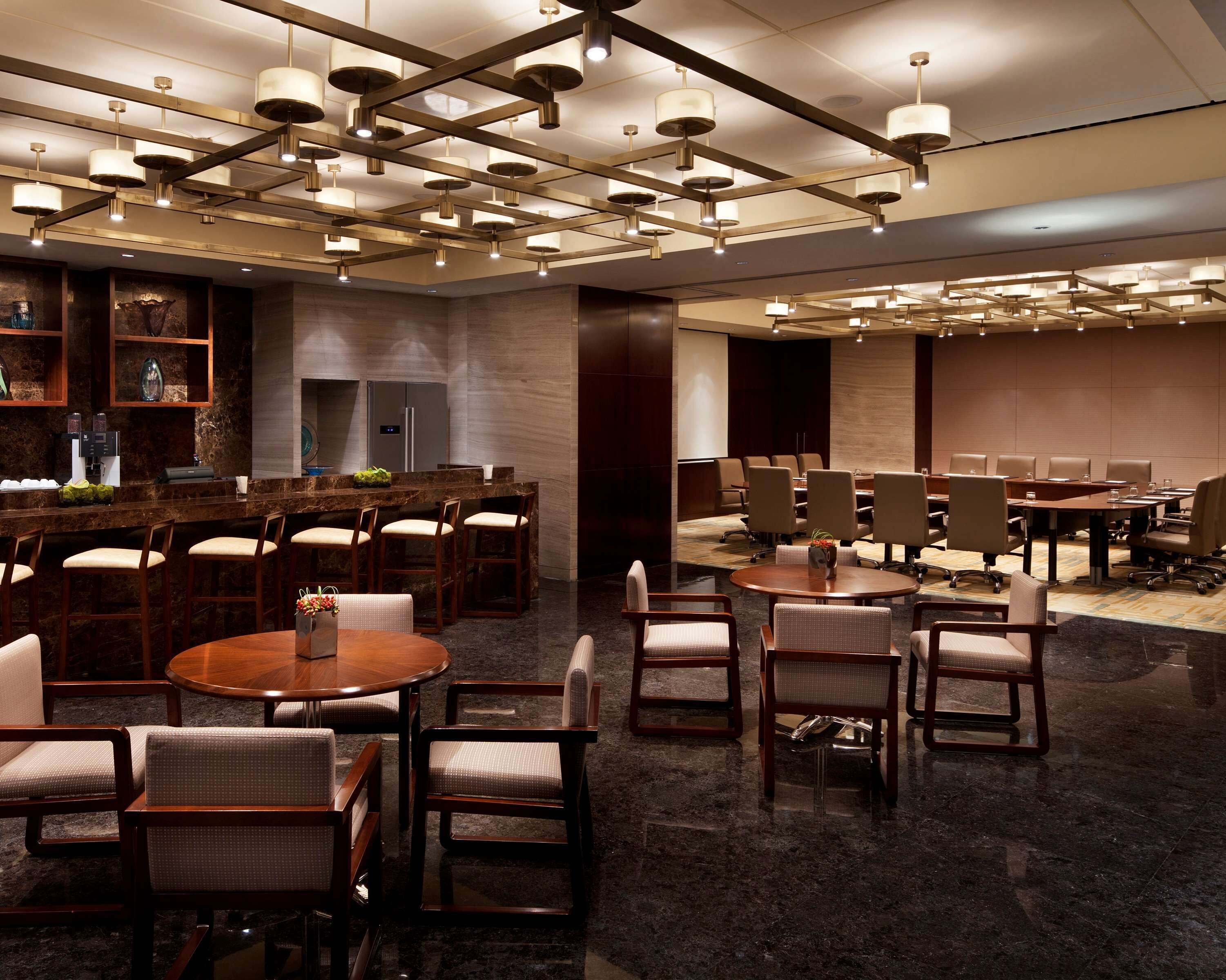 Un vestíbul d'hotel modern amb una zona de bar, taules rodones i una sala de conferències.